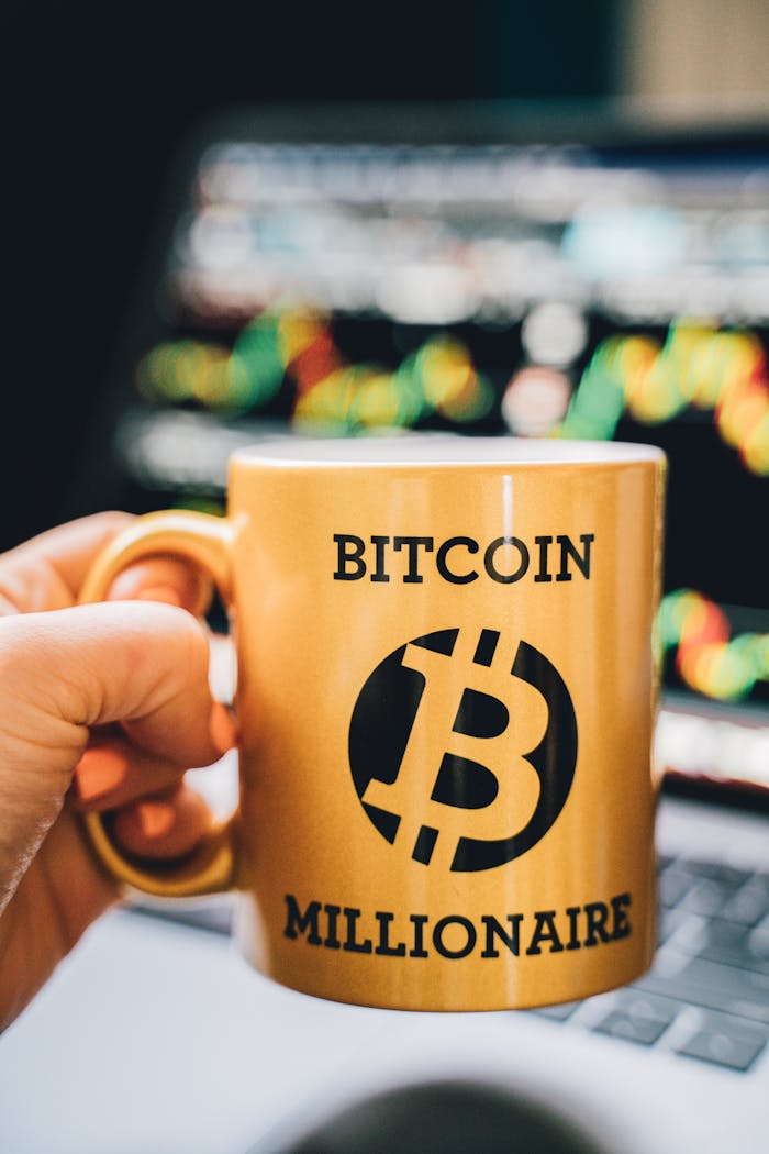 Close-up of a Bitcoin Millionaire mug held in front of a trading screen, emphasizing cryptocurrency success.