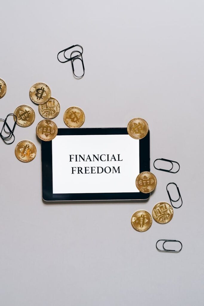 Top view of bitcoin coins and paper clips around a digital tablet displaying 'Financial Freedom'.